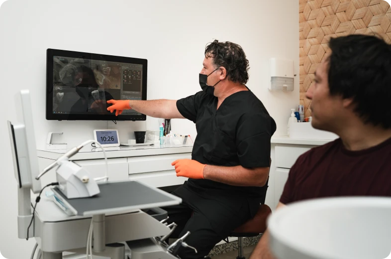 Dentiste en blouse noire expliquant une radiographie dentaire sur écran à un patient, cabinet d'endodontie Paris 16